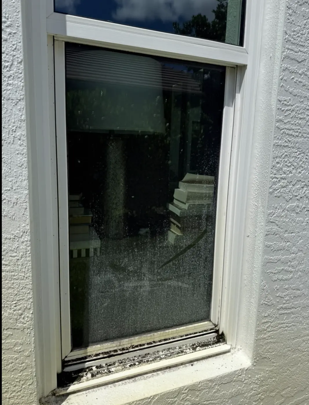 Window glass covered in spotting with a debris-filled sill before cleaning