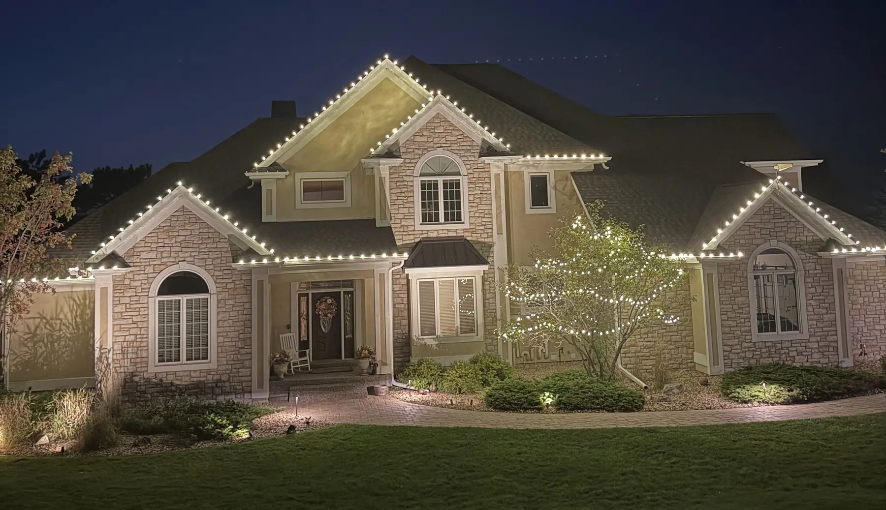 Home at night with warm white professional Christmas lights along the roofline and a lit tree