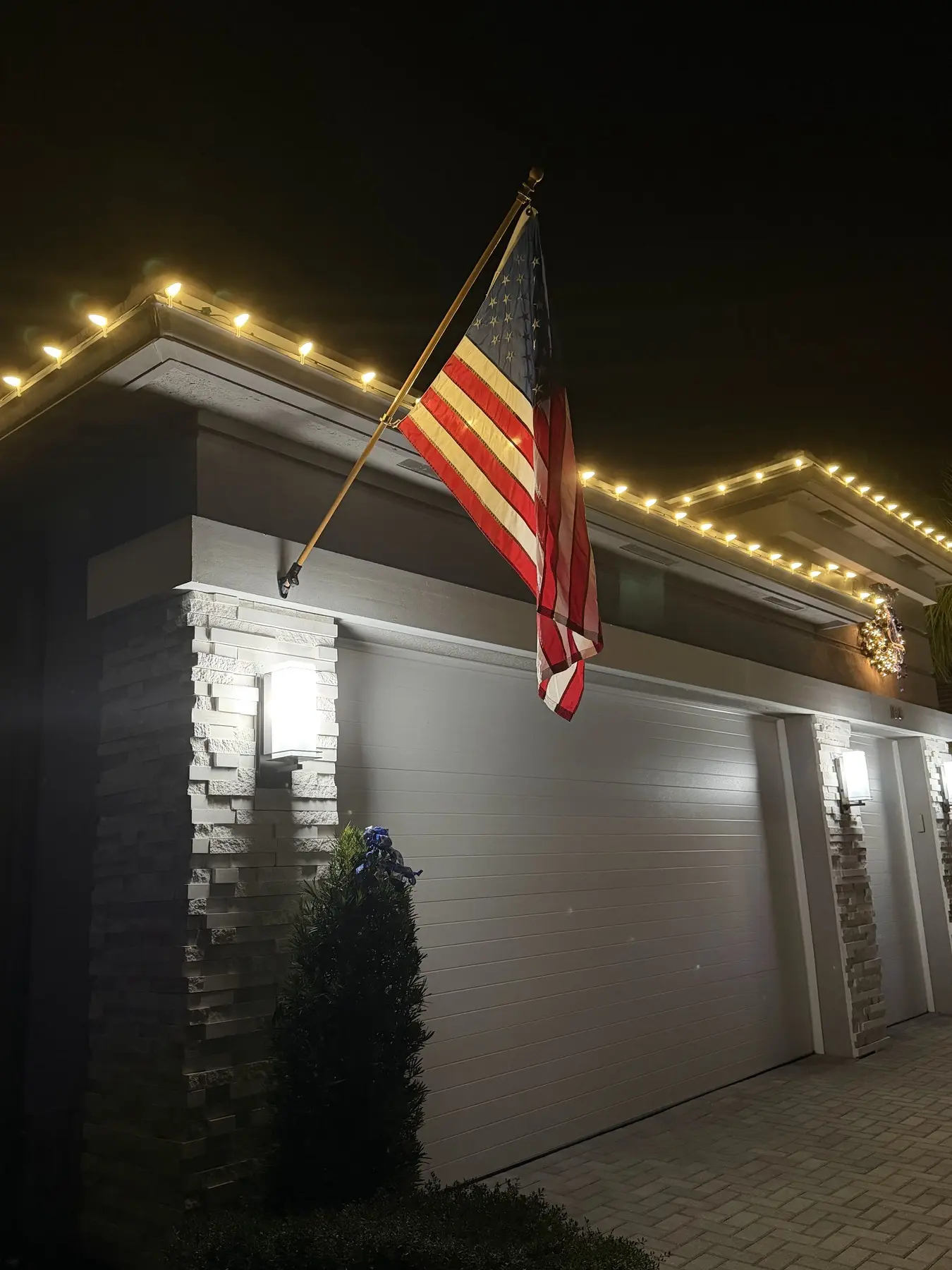 Warm white roofline lighting above a garage with an American flag